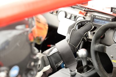 Close-up of a person wearing a protective glove while operating a VBOX product in a race car, with the dashboard, steering wheel and gear shifter visible.