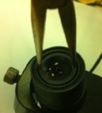 Photograph of long-nosed pliers being used to unscrew the old lens from the camera body.